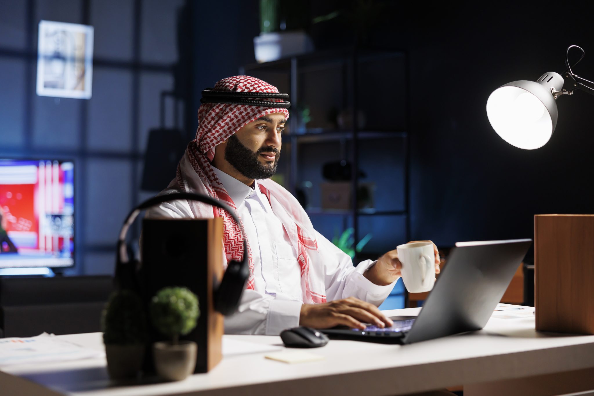 arab guy holding a cup and using laptop