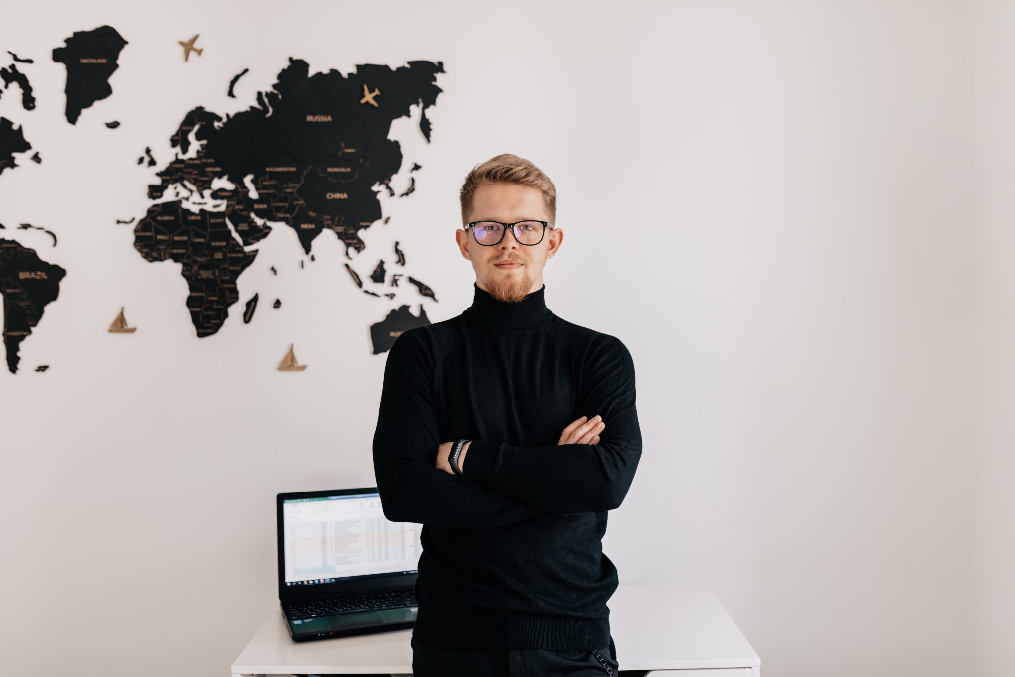 indoor portrait handsome blond man wearing spectaculars black pullover posing white wall with world map laptop desktop
